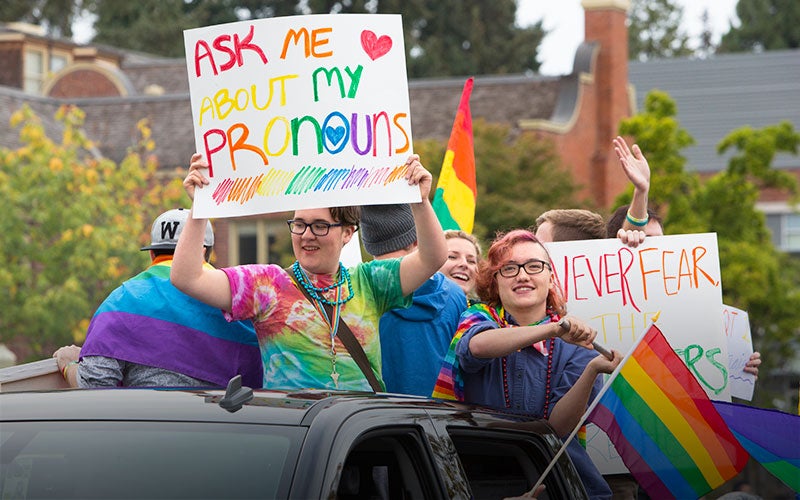 LGBTQ students show their pride with informative signs and rainbow flags on a Homecoming parade float.
